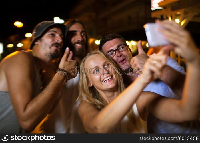 Happy friends selfie with thumbs up. Cheerful young people taking happy selfie with a mobile phone during night party. Jolly photo with thumbs up