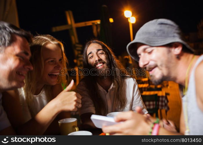 Happy friends watching photos on the cell. Group of happy friends having joyful evening in outdoor cafe and watching photos on smart phone