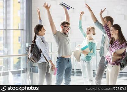 Happy friends with hands raised standing in university corridor
