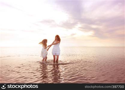 happy fun weekend by the sea - Mom and daughter in white dresses whirling by the sea at sunset. Ukrainian landscape at the Sea of Azov, Ukraine