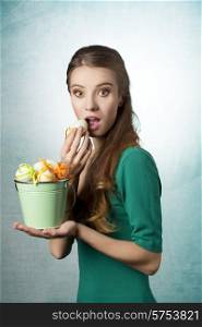 Happy, funny girl with bucket of easter eggs. She wears green dress, amd she have nice make up. She has got long, blonde hair.
