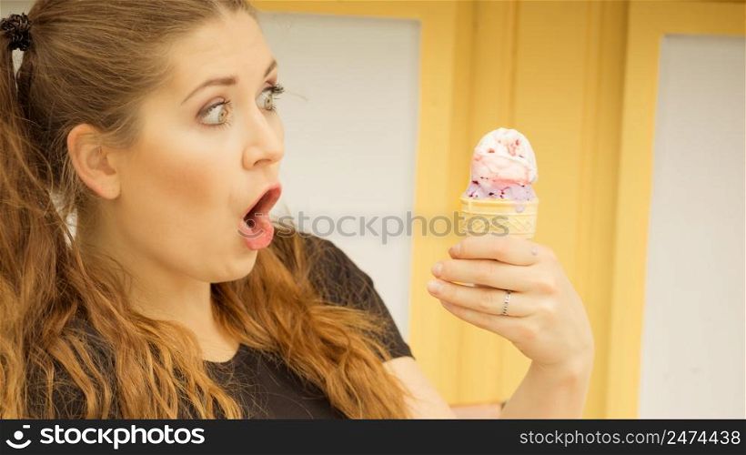 Happy funny shocked young woman with long brown hair eating ice cream having fun.. Shocked woman looking at ice cream