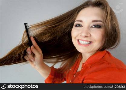 Happy funny teenage woman combing her long brown hair showing beautiful hairdo and non split ends.. Woman combing her brown hair