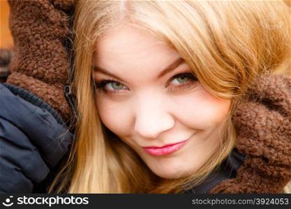 Happy funny woman wearing fashionable wintertime clothes covering her ears with big gloves