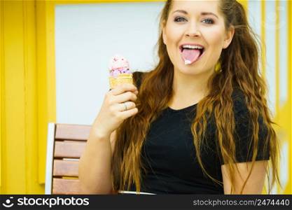 Happy funny young woman with long brown hair eating ice cream having fun.. Young woman eating ice cream