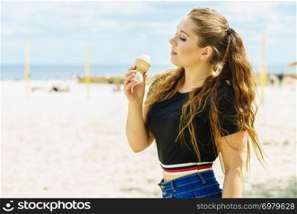 Happy funny young woman with long brown hair eating ice cream having fun on beach. Young woman eating ice cream