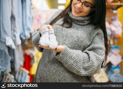 Happy future mother buys childrens clothes in the store for newborns. Pregnant woman in shop of goods for infants. Happy future mother buys childrens clothes