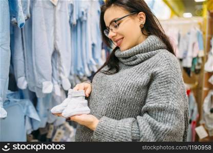 Happy future mother buys childrens clothes in the store for newborns. Pregnant woman in shop of goods for infants