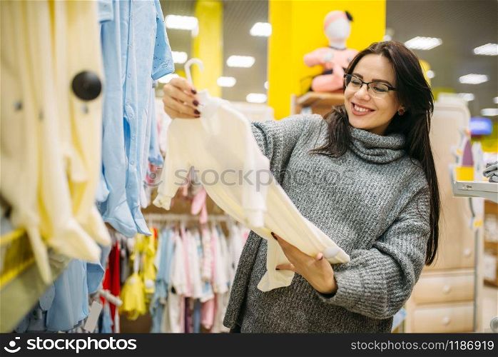 Happy future mother choosing clothes in the store for newborns. Pregnant woman in shop of goods for infants. Happy future mother choosing clothes in the store