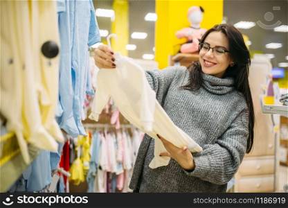 Happy future mother choosing clothes in the store for newborns. Pregnant woman in shop of goods for infants. Happy future mother choosing clothes in the store