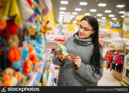 Happy future mother in glasses buys baby walkers in the store for newborns. Pregnant woman in shop of goods for infants. Happy future mother in glasses buys baby walkers