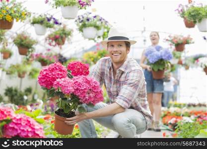 Happy gardener holding flower pot with colleague standing in background at greenhouse