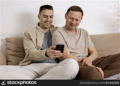 Happy gay couple with casual clothes spending time together at home and watching something on smartphone, or having video call with friends. Homosexual relationships and alternative love. Happy gay couple with casual clothes spending time together at home and watching something on smartphone, or having video call with friends. Homosexual relationships and alternative love.