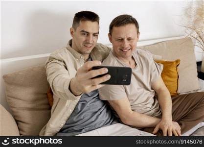 Happy gay couple with casual clothes spending time together at home and making selfie on smartphone. Homosexual relationships and alternative love. Cosy interior. Happy gay couple with casual clothes spending time together at home and making selfie on smartphone. Homosexual relationships and alternative love. Cosy interior.