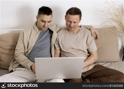 Happy gay couple with casual clothes spending time together at home and watching movie on the laptop. Two caucasian men relaxing. Homosexual relationships and alternative love. Cosy interior. Happy gay couple with casual clothes spending time together at home and watching movie on the laptop. Two caucasian men relaxing. Homosexual relationships and alternative love. Cosy interior.