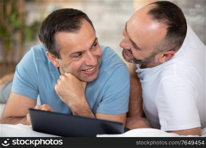 happy gay couple with tablet computer on bed at home