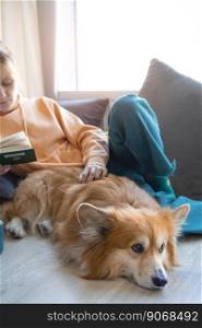 happy girl and corgi. a girl sits on the floor and reads a book next to a corgi dog 