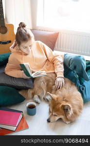 happy girl and corgi. a girl sits on the floor and reads a book next to a corgi dog 