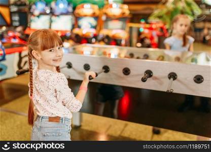Happy girl at the table soccer in children game center. Smiling female child having fun on playground indoors. Kid plays on football machine in amusement centre. Happy girl at table soccer in children game center