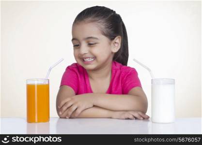 Happy girl choosing orange juice and milk against colored background