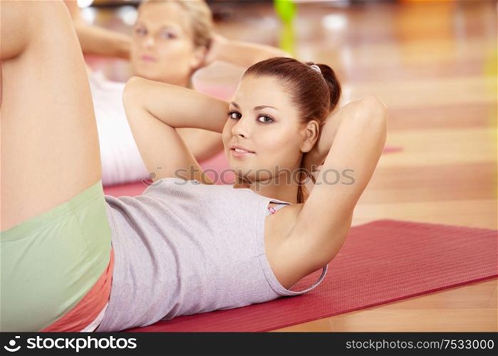 Happy girl does exercise for stomach muscles in sports club