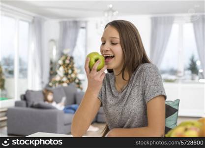 Happy girl eating apple at home