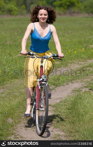 happy girl goes by bicycle on meadow