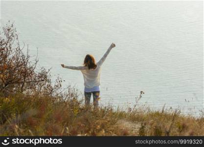 Happy girl happily raised her hands up enjoying the seascape, view from the back