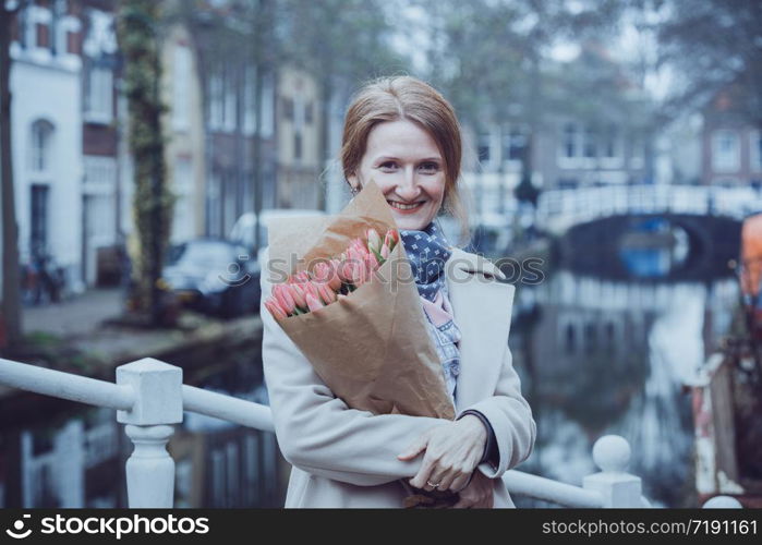 happy girl holding a bouquet of tulips standing on a street of Amsterdam. The Netherlands