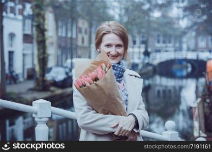 happy girl holding a bouquet of tulips standing on a street of Amsterdam. The Netherlands