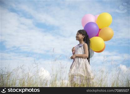 Happy girl holding colorful of balloons on a green meadow with cloudy and blue sky