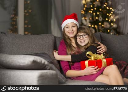 Happy girl hugging sister on sofa during Christmas
