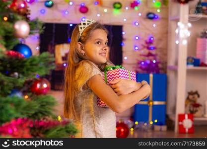 Happy girl hugs the coveted gift at the Christmas tree