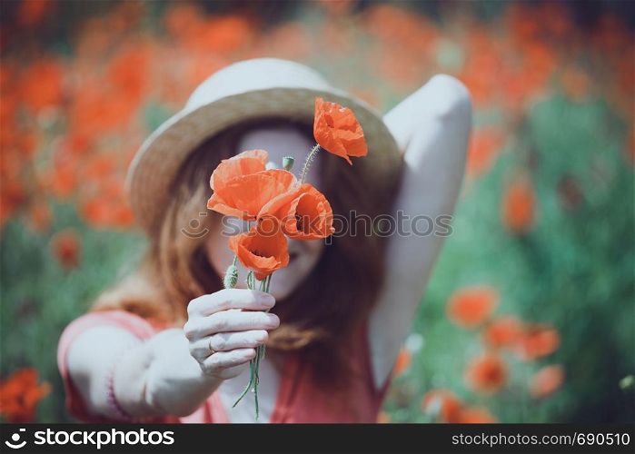 Happy girl in a hat at the amazing field of beautiful red poppy field in the countryside.