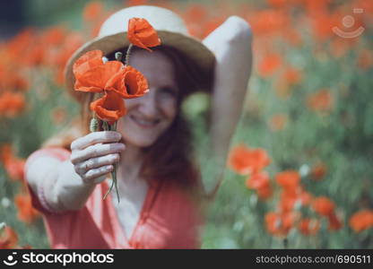 Happy girl in a hat at the amazing field of beautiful red poppy field in the countryside.