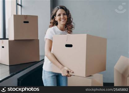 Happy girl in casual outfit is carrying box and smiling. Hispanic woman unloading and unpacking boxes. New home and independence concept. Real estate mortgage advertising mockup.. Happy girl carrying box. New home and independence concept. Real estate mortgage advertising mockup.