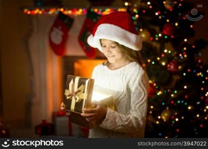 Happy girl in santa hat holding glowing present box