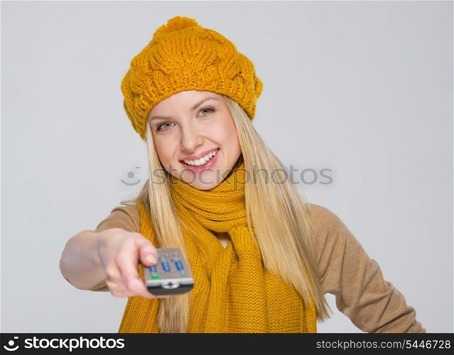 Happy girl in scarf and hat with tv remote control isolated on gray