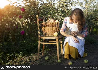 happy girl in the garden holds a rabbit in her arms and a basket of apples nearby. aesthetics of rural life