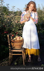 happy girl in the garden holds a rabbit in her arms and a basket of apples nearby. aesthetics of rural life 