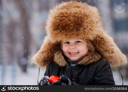 Happy girl in winter on the background of houses.. Portrait of a child in a huge winter hat 3132.