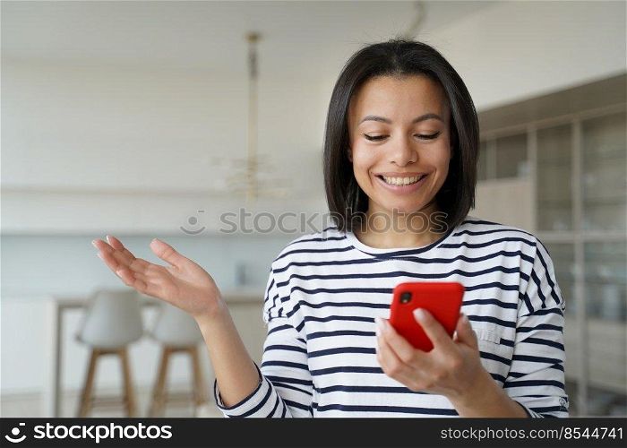 Happy girl is excited with mobile phone using. Conceptual portrait of young emotional woman holding smartphone. Pretty hispanic girl in striped casual shirt at home. Advertising banner mockup.. Happy girl is excited with mobile phone using. Smartphone advertising banner mockup.