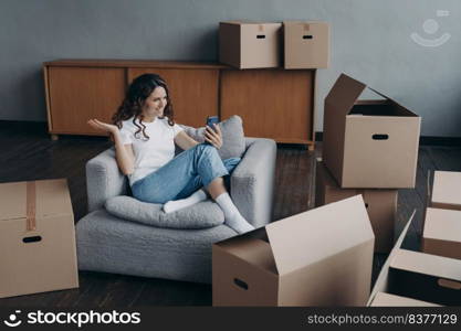 Happy girl is new apartment buyer sitting among cardboard boxes. Successful independent young woman is having video call on phone showing her dream house. Mortgage loan concept.. Happy girl having video call on phone showing her dream house. Mortgage loan concept.