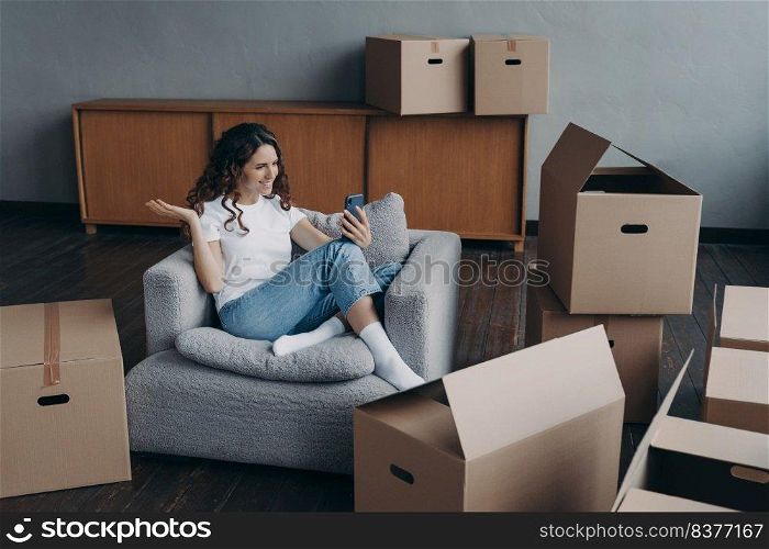 Happy girl is new apartment buyer sitting among cardboard boxes. Successful independent young woman is having video call on phone showing her dream house. Mortgage loan concept.. Happy girl having video call on phone showing her dream house. Mortgage loan concept.