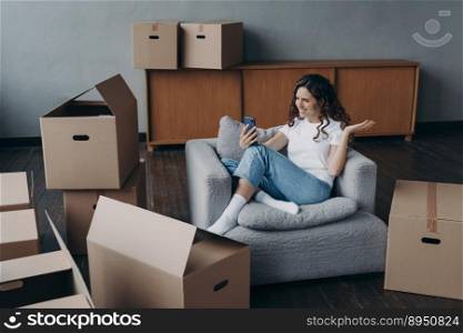 Happy girl is new apartment buyer sitting among cardboard boxes. Successful independent young woman is having video call on phone showing her dream house. Mortgage loan concept.. Happy girl having video call on phone showing her dream house. Mortgage loan concept.