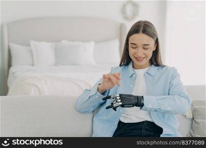Happy girl is setting her electronic bionic limb. Attractive european woman with artificial arm at home. Smiling woman has modern cyber prosthesis. Engineering and innovation concept.. Happy girl is setting her electronic bionic limb. Engineering and innovation concept.