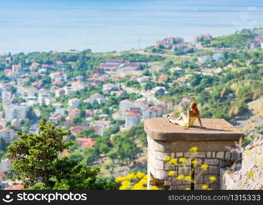 Happy girl is sitting over the city and looking to the sea