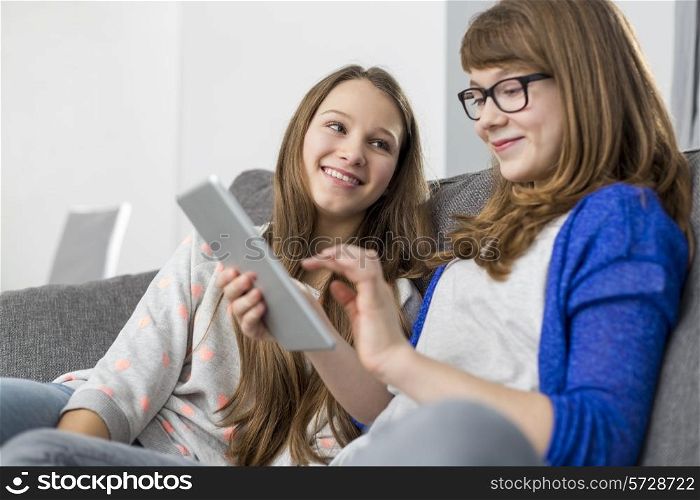 Happy girl looking at sister using digital tablet on sofa at home