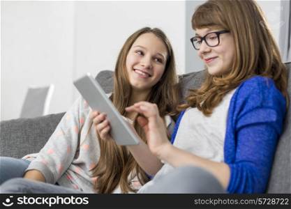 Happy girl looking at sister using digital tablet on sofa at home