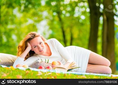 happy girl lying on the plaid with a book in a green park